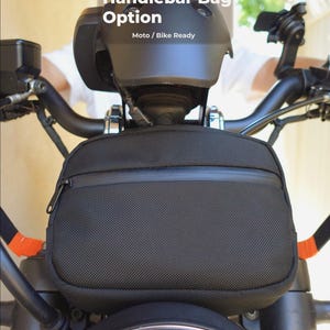 May include: Black handlebar bag with a zipper closure, mounted on a motorcycle. The bag is rectangular and has a textured surface. The text "Handlebar Bag Option" and "Moto / Bike Ready" are visible.