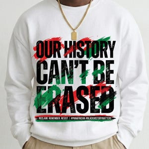 Peut inclure: Sweat-shirt blanc avec l'inscription "OUR HISTORY CAN'T BE ERASED" en noir, vert et rouge. Le design comprend des accents de coups de pinceau et les phrases "RECLAIM. REMEMBER. RESIST." et "#PANAFRICAN #BLACKHISTORYMATTERS".