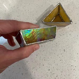 May include: Two triangular stained glass trinket dishes. One dish is iridescent with a rainbow sheen, the other is yellow. Both are framed with silver solder. The dishes are handmade and suitable for small items.