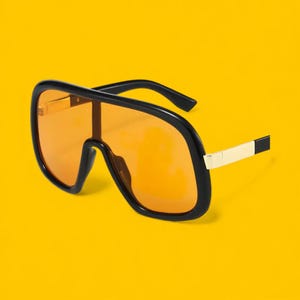May include: Oversized sunglasses with a black frame and orange lenses. The arms have a gold and black accent. The sunglasses are set against a bright yellow background.