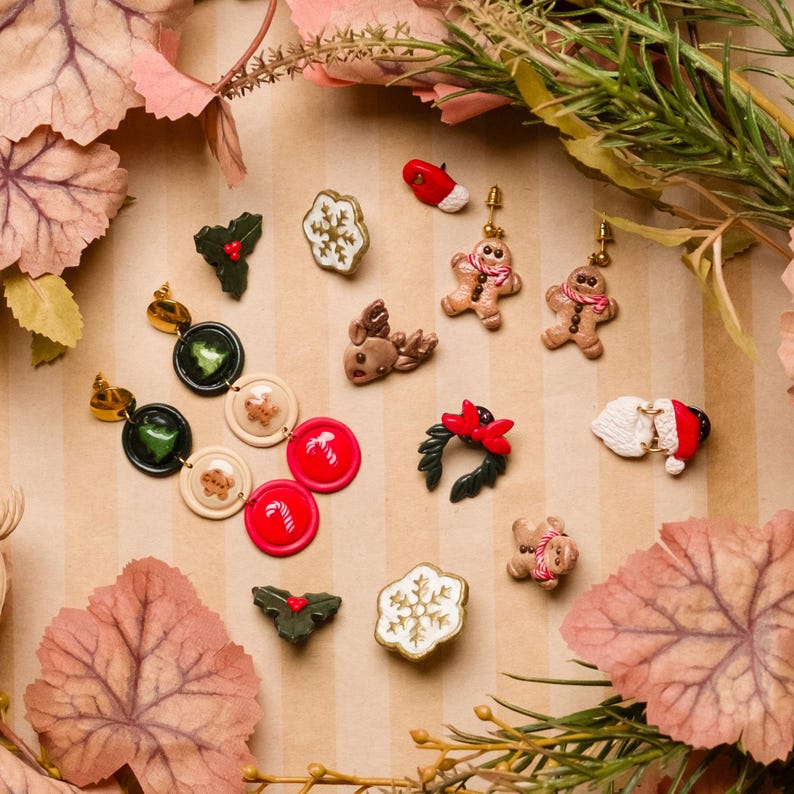 May include: A collection of Christmas-themed earrings and pins. The earrings feature gingerbread men, holly, and snowflake designs. Other pins include a reindeer, a Santa hat, and a wreath. The color palette includes red, green, white, and brown.