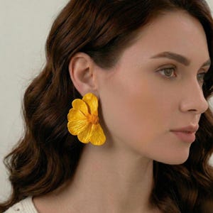 Peut inclure: Une paire de grandes boucles d'oreilles en forme de fleur jaune. Les boucles d'oreilles sont d'un jaune vif avec des textures de pétales détaillées et un centre texturé. Un accessoire audacieux.