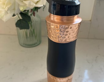 May include: A water bottle featuring a black lid with a clear straw, a hammered copper neck, a matte black central body, and a hammered copper base. The design combines metallic copper textures with a smooth black finish for a functional container.