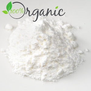 May include: A close-up of a pile of white powder against a white background. The text "100% Organic" is in the upper left corner. The powder appears to be finely ground and has a soft, textured appearance.
