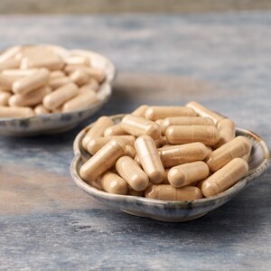 May include: Two small, round, ceramic bowls filled with beige capsules. The bowls have a blue and white speckled design. The capsules are cylindrical with rounded ends, and are a light beige color. The background is a blue-gray surface.