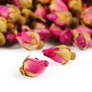 Könnte beinhalten: Nahaufnahme von getrockneten Rosenknospen, die leuchtend rosa Blütenblätter und goldbraune Kelchblätter zeigen. Die Knospen befinden sich in verschiedenen Blühstadien und bilden eine strukturierte und optisch ansprechende Anordnung. Das Bild hebt die natürliche Schönheit der Rosenknospen hervor, ideal für Tee oder Potpourri.