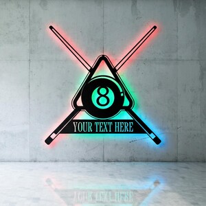Può includere: Un'insegna da biliardo nera e verde acqua con il numero 8 all'interno di un triangolo, due stecche incrociate e la scritta "YOUR TEXT HERE". L'insegna è illuminata da luci a LED rosse, verdi e blu.