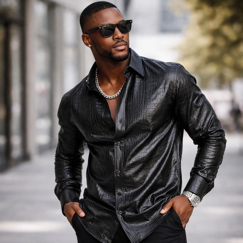 May include: A black, long-sleeved button-down shirt with a textured, crocodile-like pattern. The shirt is paired with black pants and a silver chain necklace. The person is wearing sunglasses and a silver watch.