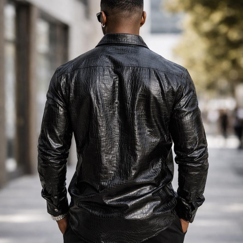 May include: A black, long-sleeved shirt with a textured, crocodile-skin pattern. The shirt has a button-down front and cuffs. The person is wearing a silver watch. The image is taken from behind, showing the back of the shirt.