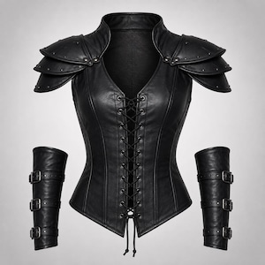 Könnte beinhalten: Ein schwarzes ärmelloses Oberteil mit Schnürung vorne, hohem Kragen und geschichteten Schulterklappen mit Metallnieten. Das Set enthält zwei passende Unterarmstulpen, die jeweils mit drei verstellbaren Riemen und Metallschnallen befestigt sind.