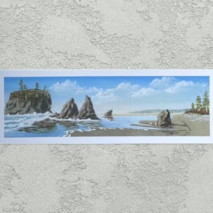 Puede incluir: Pintura de paisaje enmarcada de una escena costera. La obra representa una playa con grandes formaciones rocosas, olas rompiendo y un cielo azul con nubes. La pintura está en un marco blanco.