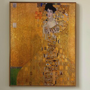 May include: A framed print of a Gustav Klimt painting, featuring a woman in an ornate gold dress against a gold background. The print is hanging above a bed with sage green bedding. The text "APOLLO TIMELESS PRINTS" is in the upper right corner.