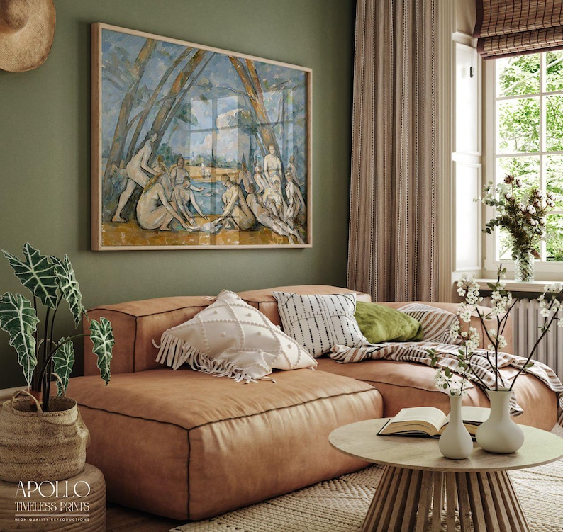 May include: A living room scene featuring a large framed artwork depicting figures near water, above a brown leather sectional sofa. Decorative pillows in white, black, and green adorn the sofa. A round wooden coffee table and potted plants complete the cozy setting.