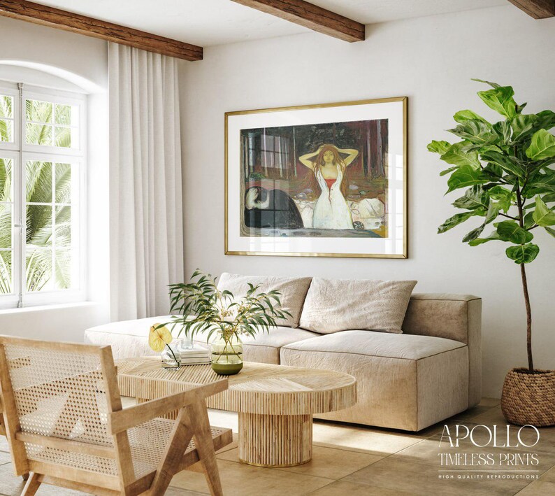 May include: A living room scene featuring a framed artwork with a gold frame, a beige sectional sofa, and a wooden coffee table. A large green plant in a woven basket sits in the corner. The room has a neutral color palette with natural light.