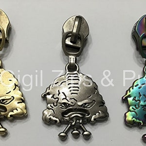 May include: Three zipper pulls with a cartoon monster design. The pulls are in gold, silver, and iridescent colors.