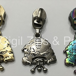 May include: Three zipper pulls with a cartoon monster design. The pulls are in gold, silver, and iridescent colors.