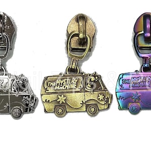 May include: Three metal zipper pulls featuring the Mystery Machine from Scooby Doo. The zipper pulls are in silver, gold, and a rainbow iridescent finish.