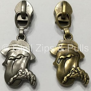 May include: Two zipper pulls with a tongue and hat design. One pull is silver and the other is gold.