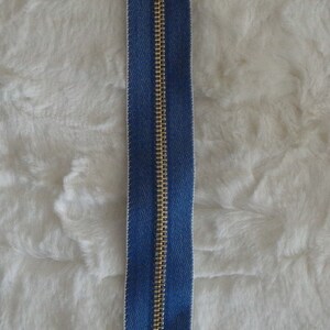 May include: A gold zipper with a blue denim tape. The zipper pull is a gold skull.