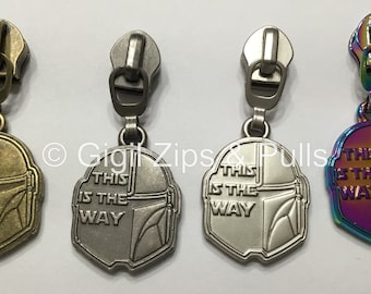 Op de afbeelding: Vier ritsen met een Mandalorian helm ontwerp en de tekst "This is the way". De ritsen zijn verkrijgbaar in vier afwerkingen: antiek messing, zilver, nikkel en iriserend.