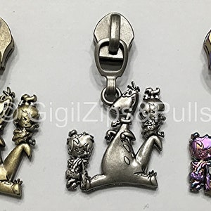 May include: Three zipper pulls featuring a cartoon dinosaur and a small human character. The pulls are in three different finishes: antique brass, silver, and iridescent purple.