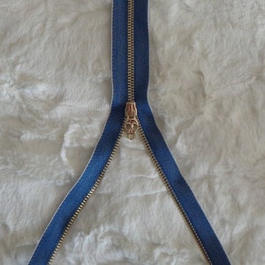 May include: A gold zipper with a blue denim tape. The zipper is open and the slider is in the middle.
