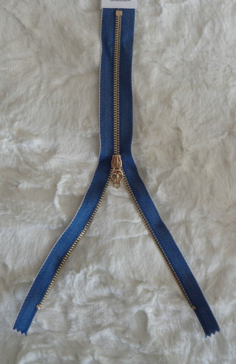 May include: A gold zipper with a blue denim tape. The zipper is open and the slider is in the middle.