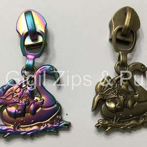 May include: Two zipper pulls, one with a rainbow iridescent finish and the other in antique brass. Both feature a cartoon character riding a flamingo.