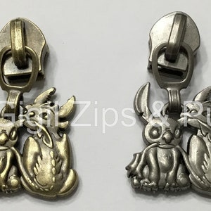 May include: Two zipper pulls featuring a cartoon character with large ears and a dragon. The zipper pulls are available in antique gold and silver finishes.