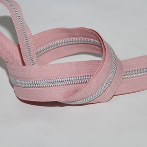 May include: A pink zipper with a silver iridescent zipper tape. The zipper is coiled and ready for sewing.