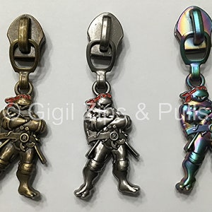 May include: Three zipper pulls featuring a Teenage Mutant Ninja Turtles character. The pulls are in three different finishes: gold, silver, and iridescent.