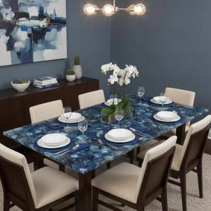 Puede incluir: Un juego de comedor con una mesa de piedra de ágata azul y seis sillas. La mesa está puesta con platos blancos, manteles individuales azules y cubiertos. Un centro de mesa de orquídeas blancas se encuentra en el centro de la mesa. Las sillas tienen asientos color crema y marcos de madera oscura.