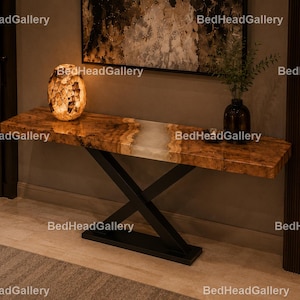 May include: A console table featuring a live-edge wood slab with a central translucent resin inlay, supported by a black metal X-shaped base. The tabletop displays natural wood grain patterns and is illuminated by a glowing, textured lamp.