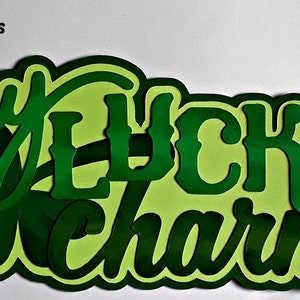 May include: Green paper cut-out of the phrase "my lucky charm" with a shamrock in the middle. The letters are layered and have a 3D effect. The cut-out is 16.5 cm by 7.6 cm.