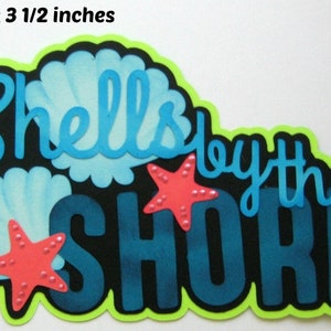 May include: A blue and green paper craft with the text "Shells by the Shore" and two pink starfish with white dots. The craft is 5 1/2 inches by 3 1/2 inches.