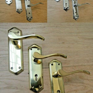 May include: A collection of six door handles with backplates, featuring three polished chrome sets and three polished brass sets. Each handle has a curved lever design and a rectangular backplate with pointed ends, including variations with and without keyholes.