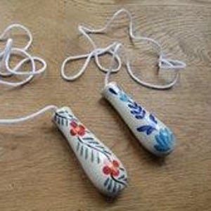 Peut inclure: Deux poignées coniques en céramique pour interrupteur à tirette, dotées d'une base blanche avec des motifs floraux peints à la main en rouge, bleu et vert. Chaque poignée est fixée à un cordon blanc pour actionner un plafonnier ou un ventilateur.