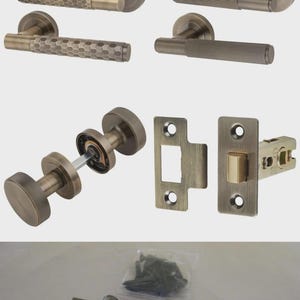 Könnte beinhalten: Ein Set aus antiken Messing-Türbeschlägen, bestehend aus zwei Drückergarnituren mit Wabenmuster, zwei geriffelten Drückergarnituren, einem runden Knaufset, einem Schließblech, einem Schloss mit der Aufschrift Elite und zwei Scharnieren mit Schrauben.