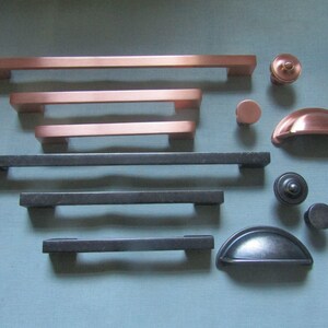 May include: A collection of cabinet hardware including three copper-toned bar pulls, three dark grey bar pulls, two round knobs, two cup pulls, and a small plastic bag containing several metal screws for installation purposes.