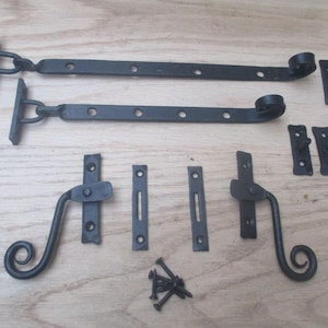 May include: A set of black metal hardware including two long strap hinges with curled ends, two matching latch handles with scroll details, four small mounting plates, and a small pile of black screws for installation on doors or shutters.