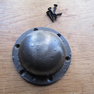 May include: A circular, dark gray, textured metal dome-shaped hardware piece with a flat outer rim featuring six pre-drilled screw holes. The item is accompanied by four small, black, threaded metal screws for installation purposes.