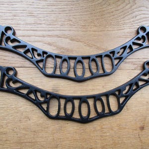 May include: Two matching black metal handles with an arched, openwork design. Each handle features a series of oval and geometric cutouts along the curved frame, with circular attachment points at both ends for secure mounting hardware.