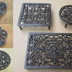 Könnte beinhalten: Eine Sammlung von Topfuntersetzern aus dunkelgrauem Gusseisen in verschiedenen Formen, darunter Herz-, Blumen-, Oval-, Quadrat- und Rechteckdesigns. Jedes Stück weist aufwendige durchbrochene Schnörkelmuster und erhöhte Metallfüße auf.