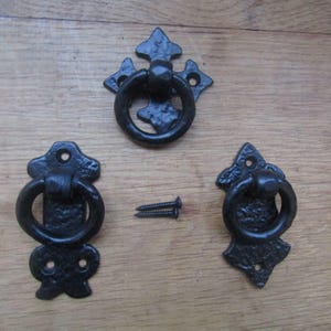 May include: Three black metal ring pulls with textured surfaces and decorative backplates. Each pull features a circular ring attached to a mounting plate with pre-drilled screw holes. Two small black metal screws are included in the centre.