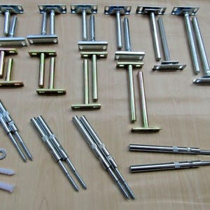 May include: A collection of metal hardware components including various T-shaped shelf brackets with mounting plates, several long cylindrical threaded support rods, two small circular metal washers, and two white plastic wall anchors.