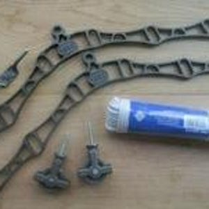 May include: Two dark brown, arched metal support brackets with an openwork design, two small metal pulleys with threaded bolts, a small metal fastener, and a roll of white cord wrapped in blue and white plastic packaging for assembly.