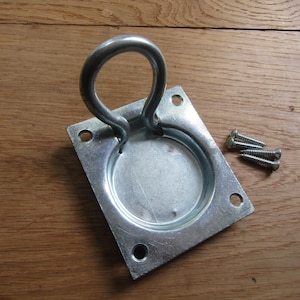 May include: A silver-colored metal recessed pull handle featuring a square base plate with four mounting holes and a hinged D-shaped ring. The hardware includes three small silver-colored metal screws with threaded shanks for installation.