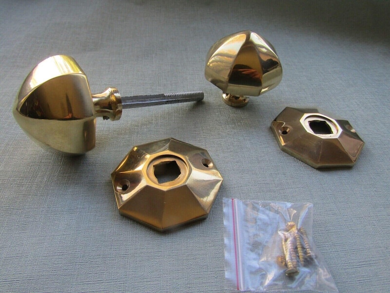 Puede incluir: Dos pomos de puerta de lat&oacute;n pulido con forma geom&eacute;trica facetada, acompa&ntilde;ados de dos placas de montaje octogonales a juego y una peque&ntilde;a bolsa de pl&aacute;stico transparente que contiene varios tornillos met&aacute;licos para la instalaci&oacute;n.