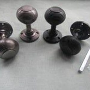 Può includere: Quattro pomelli per porta in metallo scuro con un design sferico scanalato e piastre di montaggio circolari. Ogni pomello presenta uno stelo centrale e una superficie testurizzata con scanalature. Sono inclusi un perno e un sacchetto di viti.