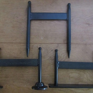 May include: Three black metal H-shaped structures with vertical posts and horizontal bars. One structure has pointed ends, one has circular bases, and one has a flat rectangular base. Each horizontal bar features embossed text reading Steelworks 1950.